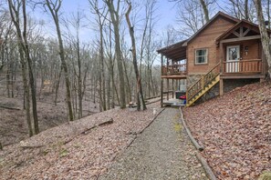 A wooden cabin with a balcony, surrounded by a forest.