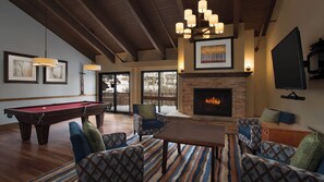 A cozy living room with a pool table, comfortable seating, a fireplace, and a large window overlooking a snowy landscape. - Beautiful Villa At Marriott Evergreen Sleeps 8 (Vail)
