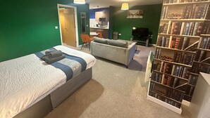 A room with a bed, a sofa, a bookshelf, and a TV.