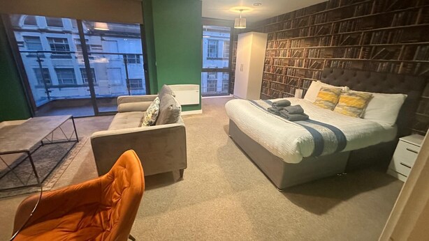 A modern bedroom with a large bed, a sofa, a chair, and a bookshelf.