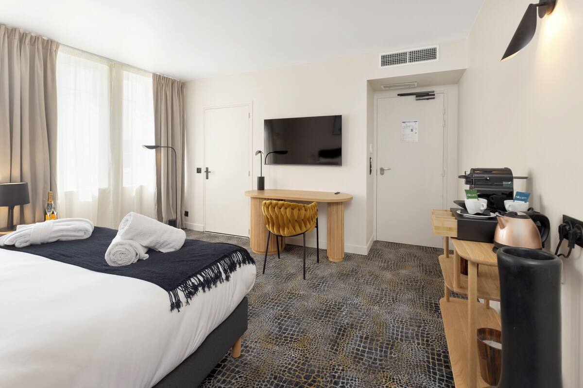 Une chambre d’hôtel équipée d’un lit, d’un bureau, d’une télévision et d’un coin café.