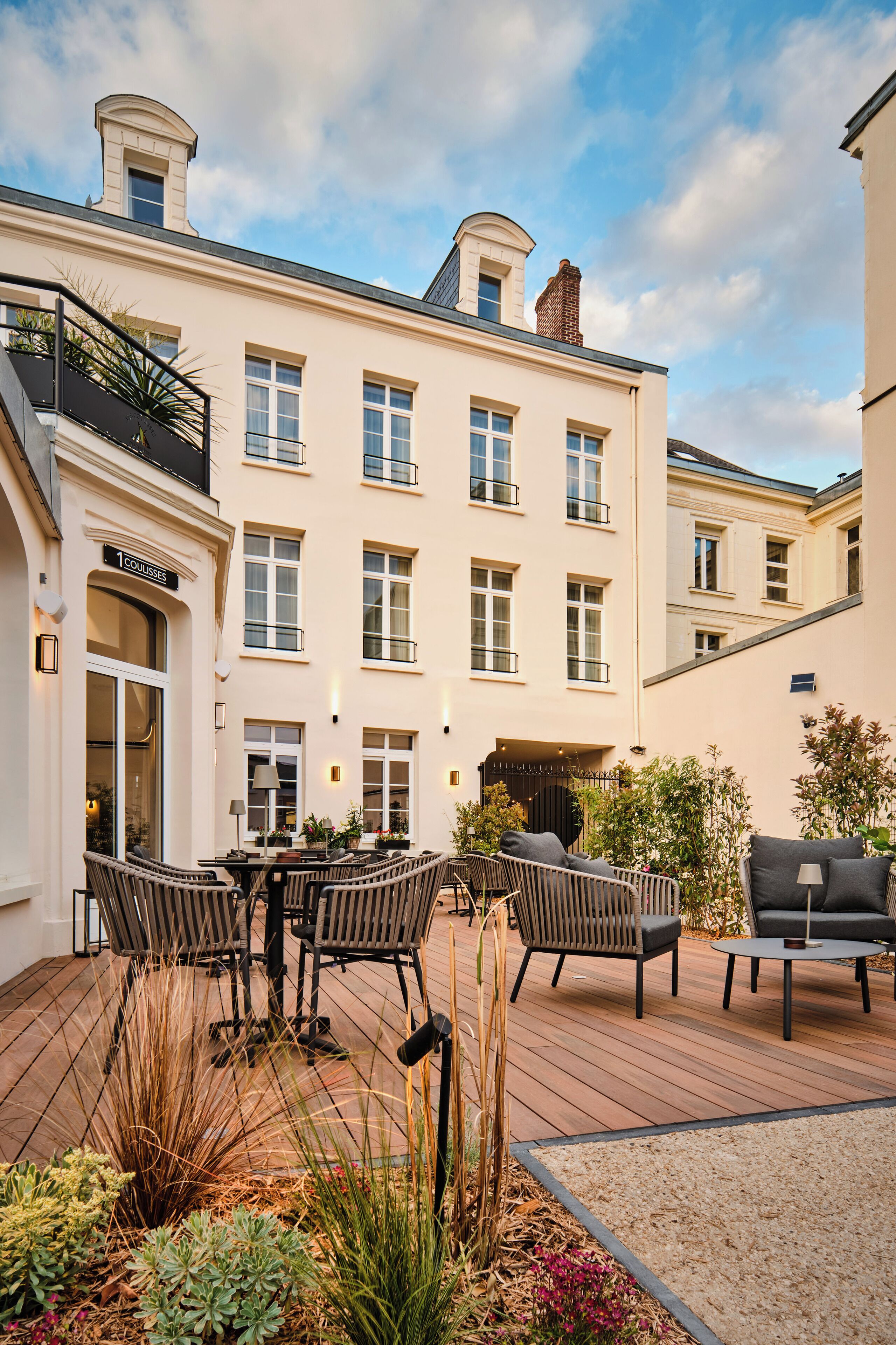 A courtyard with outdoor seating, a building with multiple windows, and a sign that reads "ECOLES."