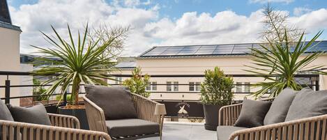 Una terraza en la azotea con mobiliario de mimbre, plantas en macetas y un panel solar.