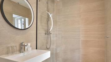 A modern bathroom with a large mirror, a shower, and a sink with toiletries.