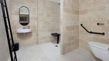 Une salle de bain avec des carreaux de couleur beige, un lavabo blanc, un miroir, des toilettes et une barre d’appui noire.