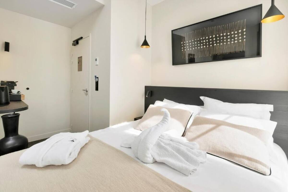 Une chambre d’hôtel avec un lit, des serviettes blanches, une tête de lit noire, une œuvre d’art accrochée au mur et une petite table avec une lampe.