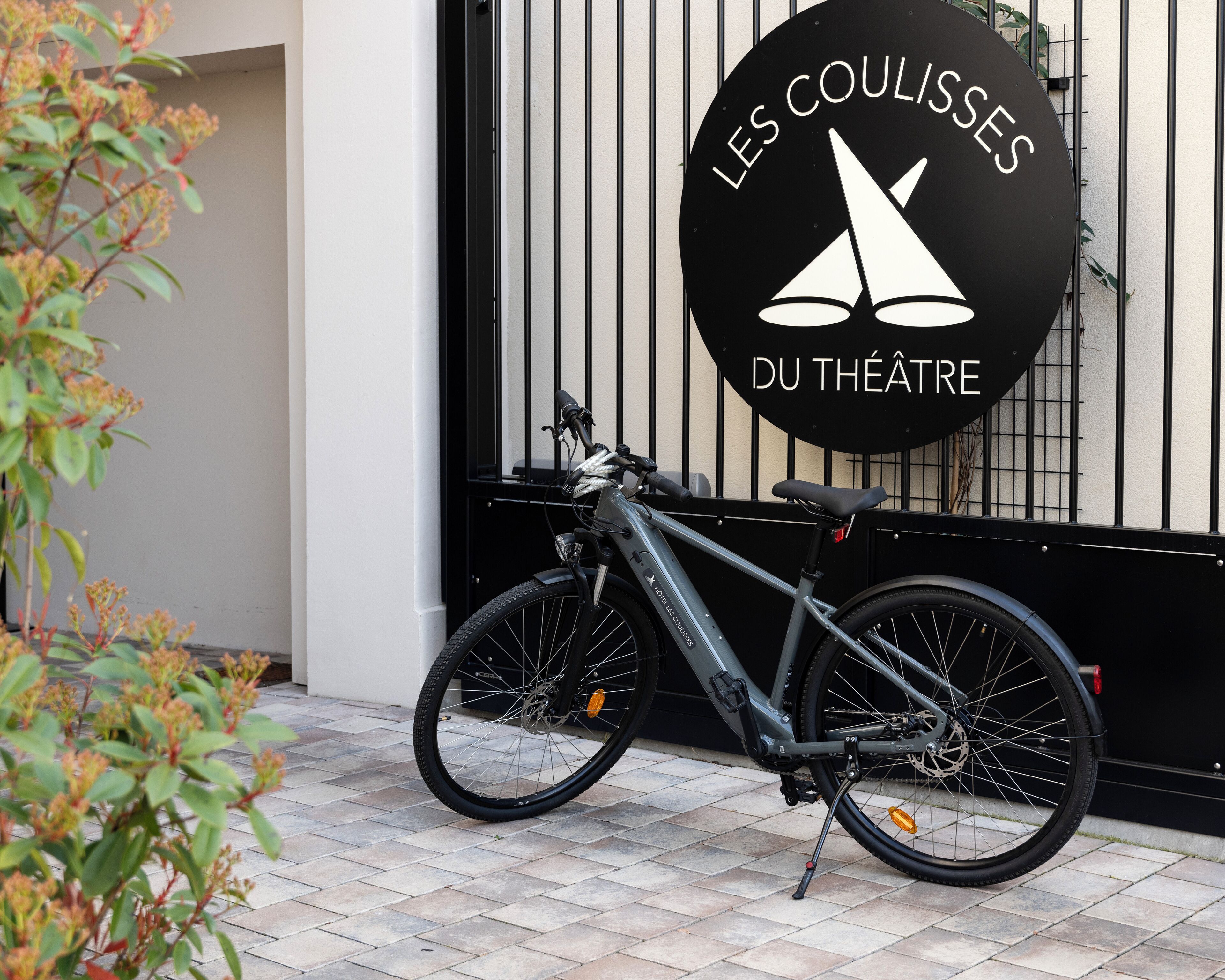 Un vélo est garé devant un bâtiment sur lequel on peut lire l’inscription : « LES COULISSES DU THÉÂTRE ».