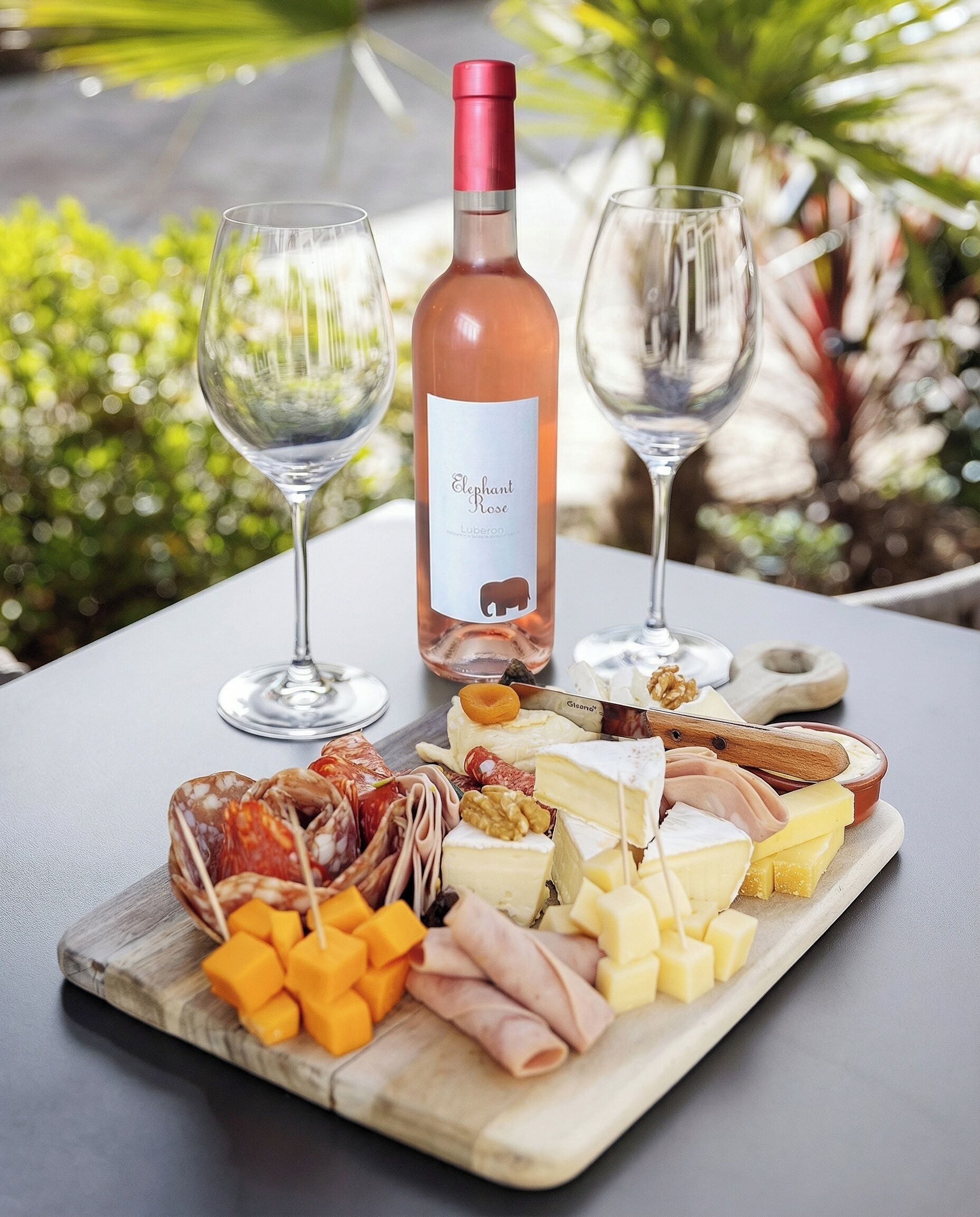 Une table avec une bouteille de vin, deux verres et une planche de charcuterie comprenant différents fromages et différentes sortes de viande.