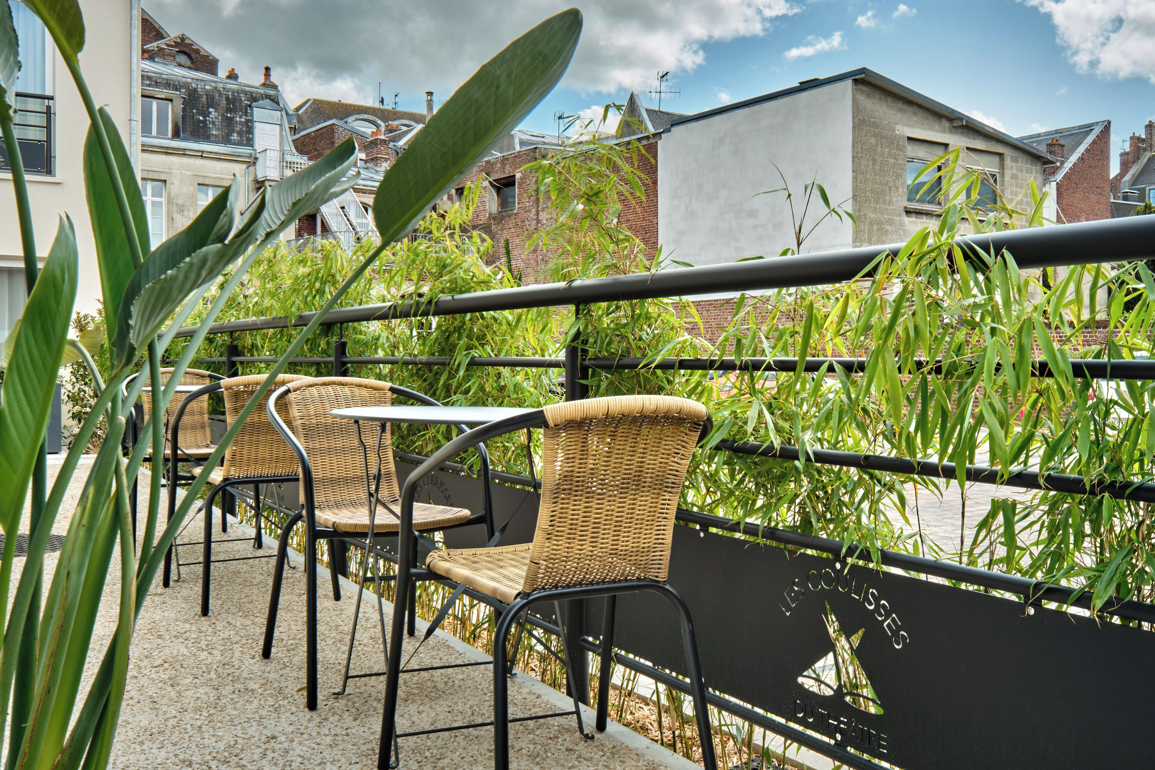 A terrace with wicker chairs and a table, overlooking a river and buildings.