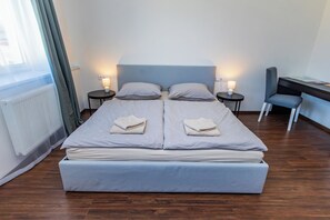 A double bed with two pillows, a bedside table with a lamp, a desk with a chair, and a window with curtains. - Prague Legends Pension (Prague)