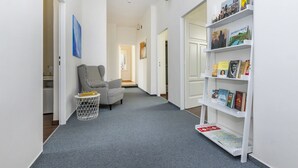 A hallway with a checkered armchair, a small side table, and a bookshelf filled with books and travel guides. - Prague Legends Pension (Prague)