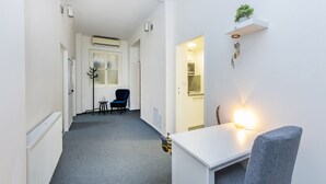 A hallway with a white radiator, a coat rack, a blue chair, a small table, and a wall-mounted shelf with a plant. - Prague Legends Pension (Prague)