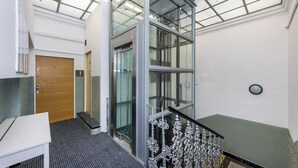 A modern interior with a glass elevator, a wooden door, and a staircase with ornate metal railings. - Prague Legends Pension (Prague)