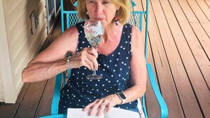 A person sitting at a turquoise metal table with an open book, on a wooden deck.