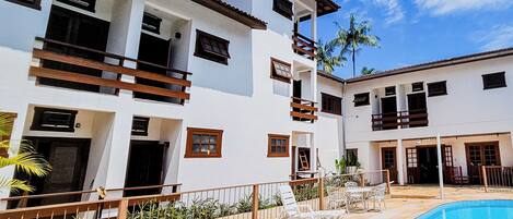 Un edificio moderno de dos pisos con piscina, mobiliario exterior y un patio cercado.