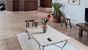 Un vaste espace de vie doté d’un haut plafond, d’un comptoir d’accueil en bois, d’une grande plante en pot, d’un tapis blanc et d’un banc.