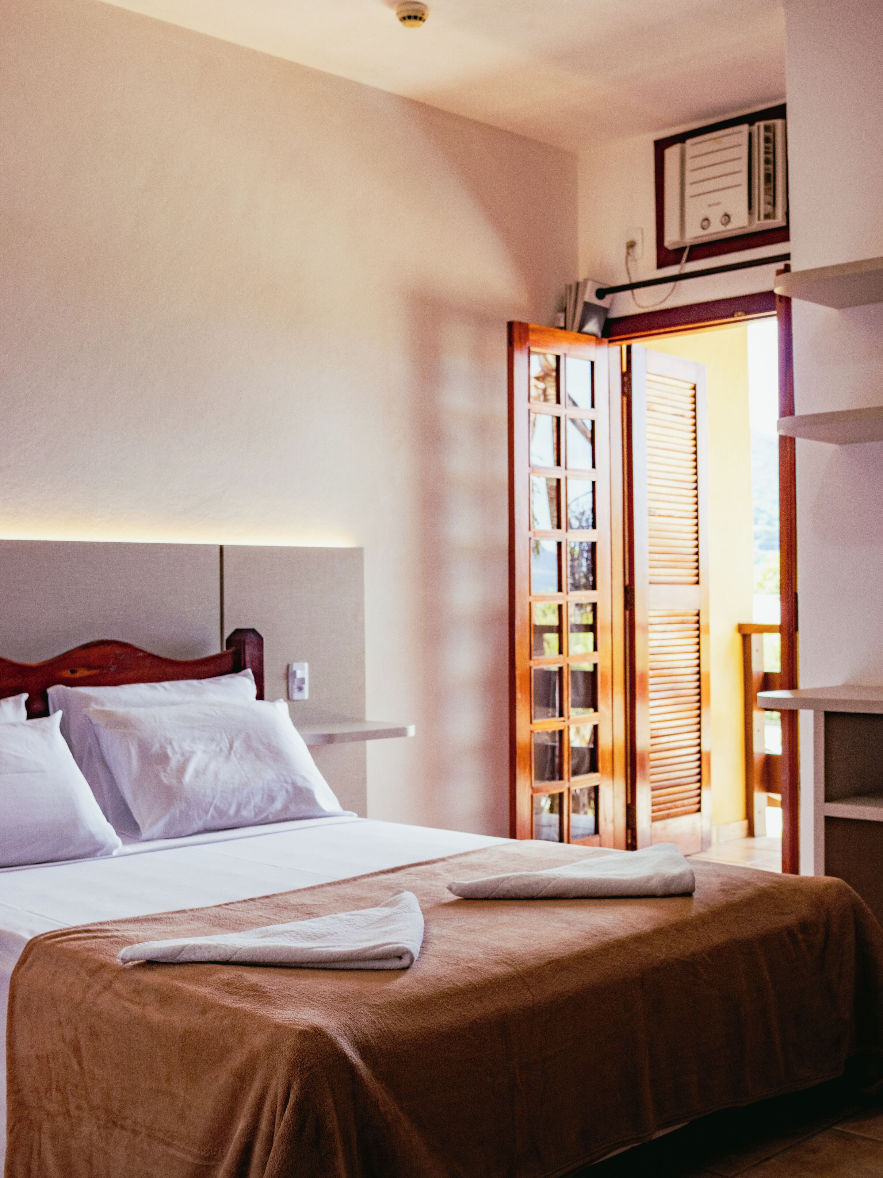 Una habitación de hotel con cama, cabecero de madera, mesita de noche y armario con puerta corredera.