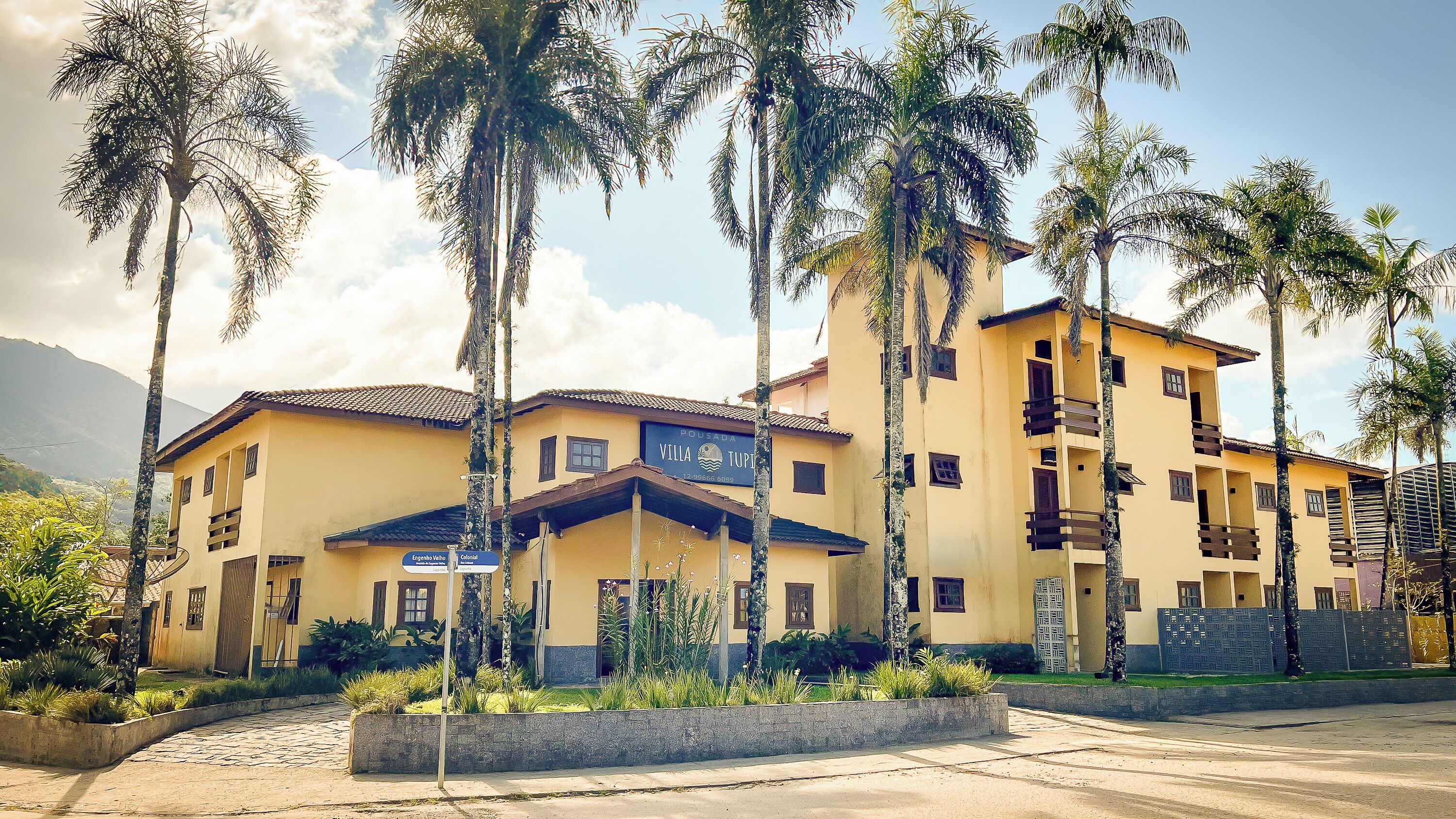 Un hotel de varios pisos con fachada amarilla, balcones y un letrero que indica las áreas 'Engenho Vale' y 'Colonal'.