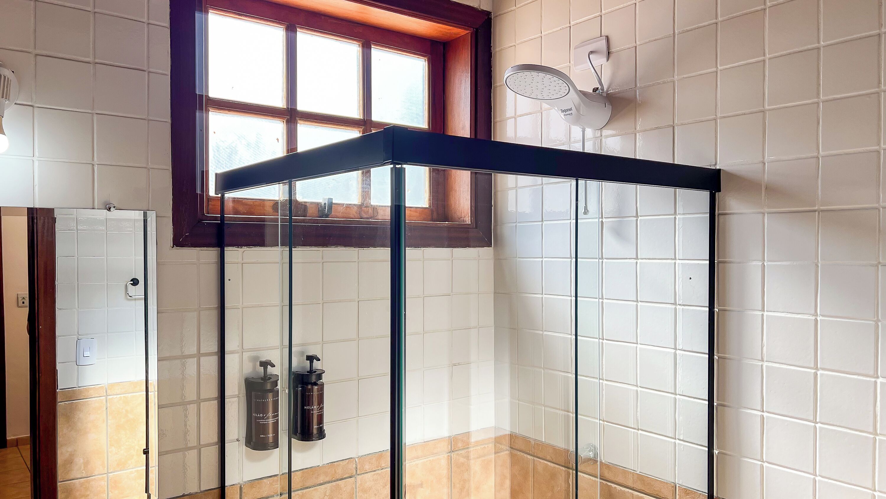 Un baño con cabina de ducha de vidrio, una ventana y dos dispensadores de jabón para manos.