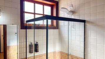 A bathroom with a glass shower enclosure, a window, and two hand soap dispensers.