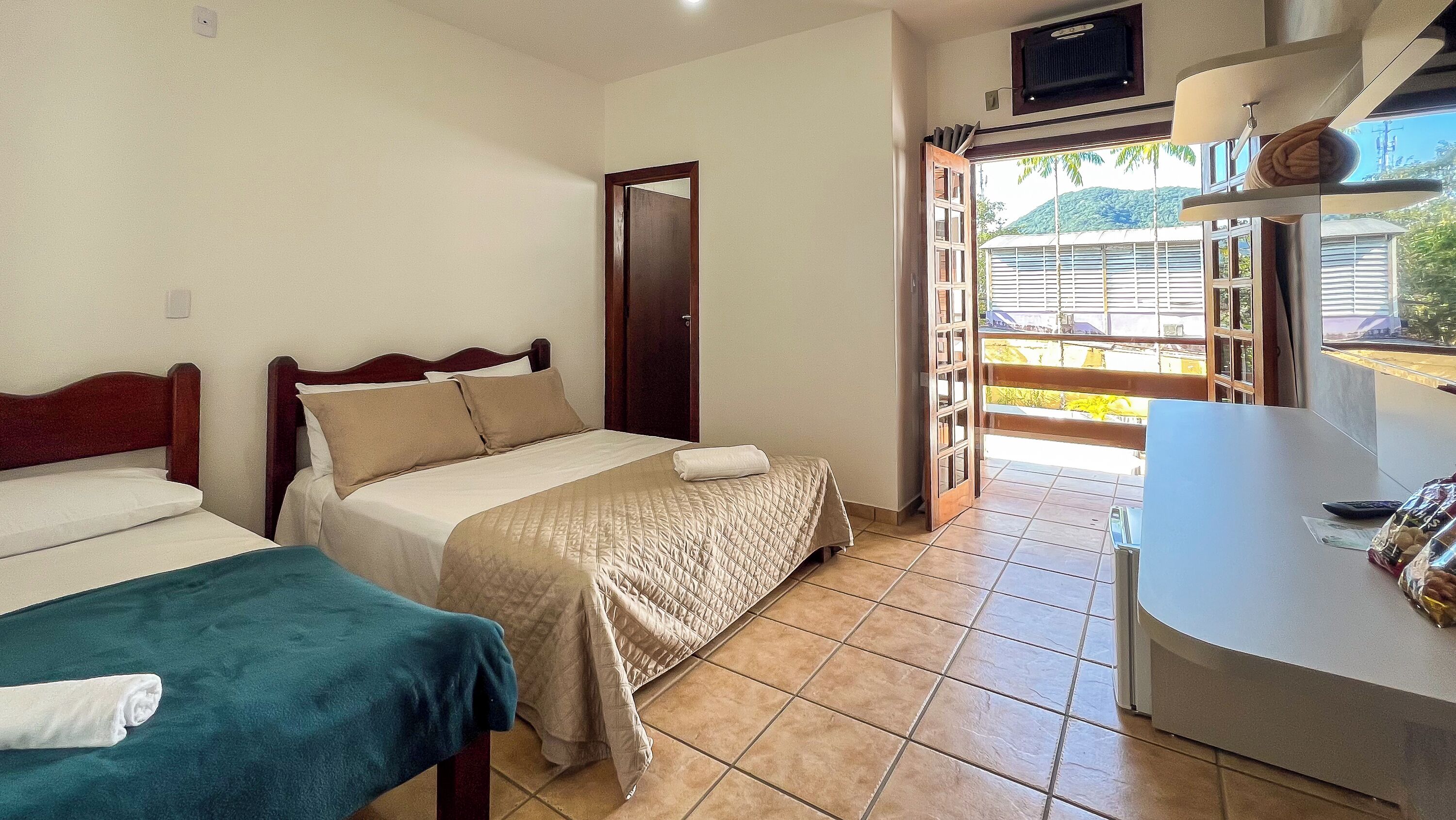 Habitación de hotel con dos camas, una mesita y vistas al exterior.