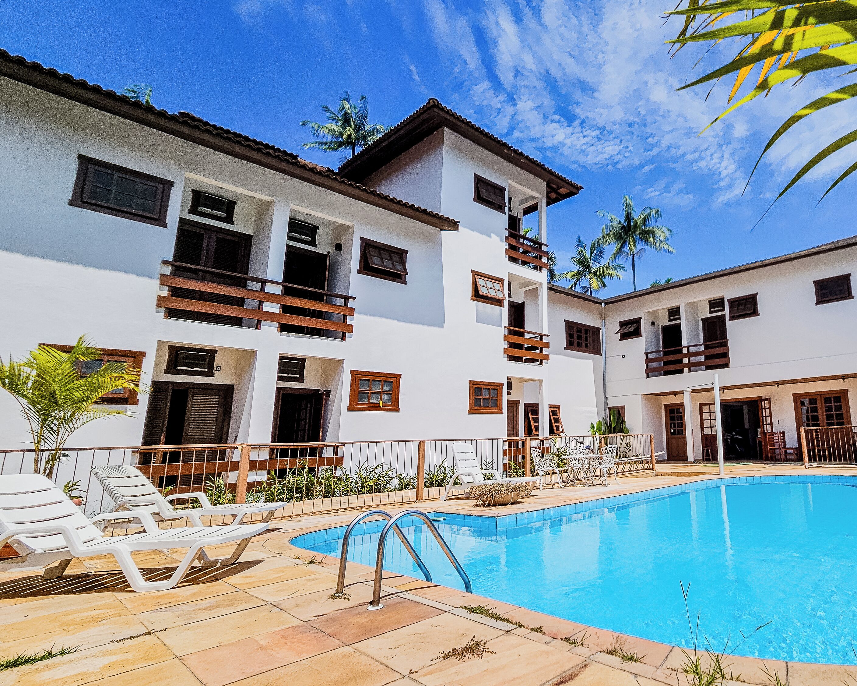 A two-story building with a swimming pool, outdoor seating, and palm trees.