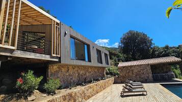 Relax in a serene outdoor space surrounded by lush greenery and trees, featuring a swimming pool and wooden deck.