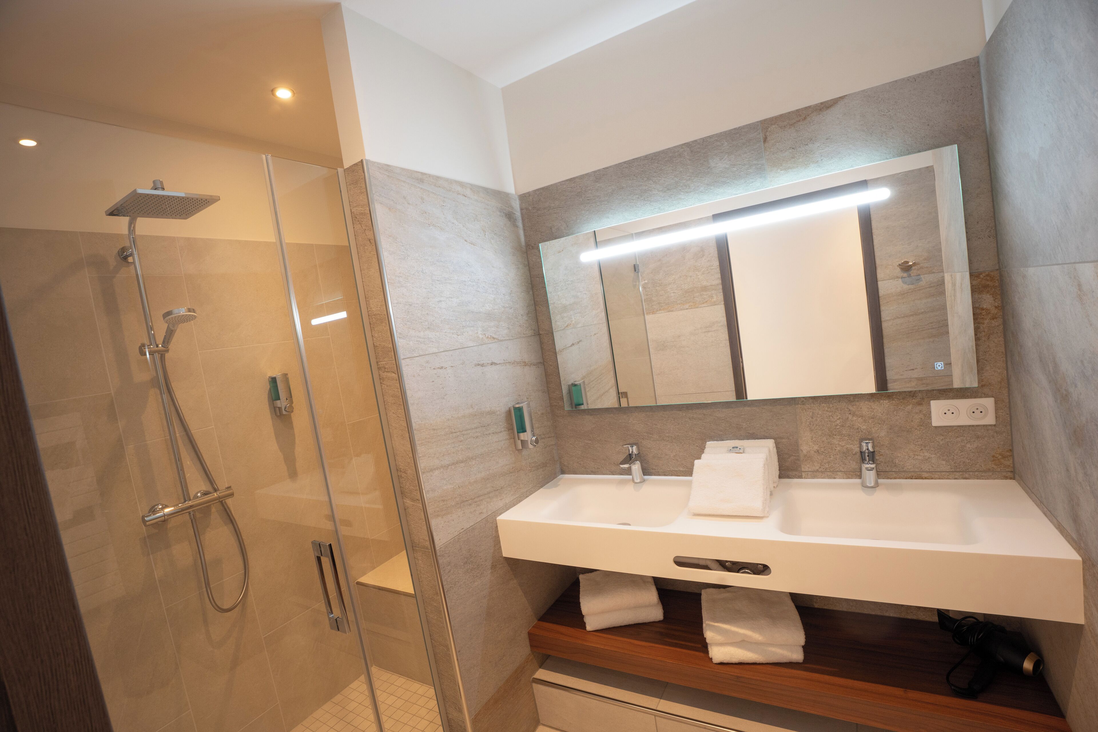 A modern bathroom with a glass-enclosed shower, a large mirror, and a white sink with a wooden vanity.