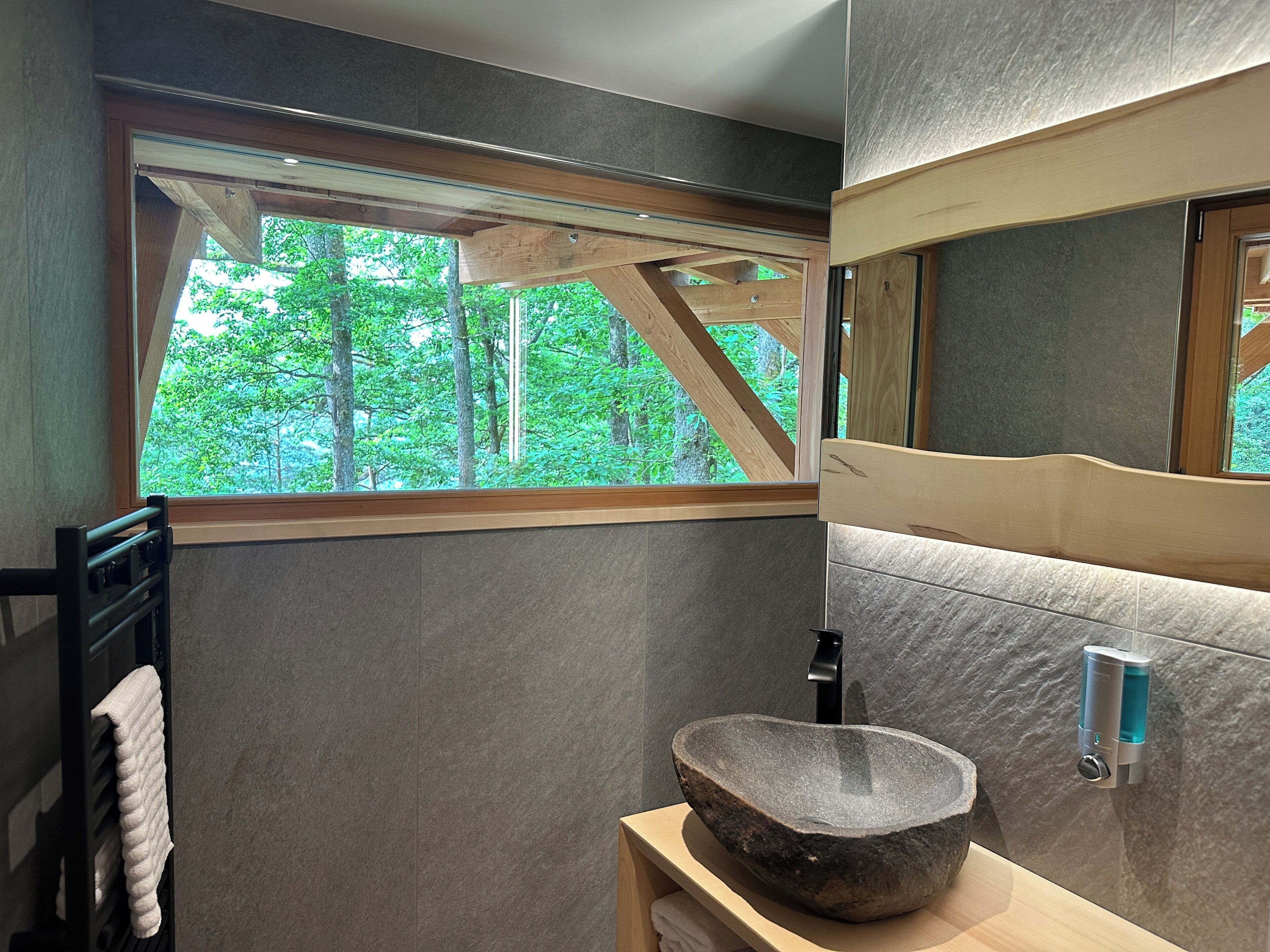 A bathroom with a stone sink, a towel rack, a mirror, and a window with a view of trees.