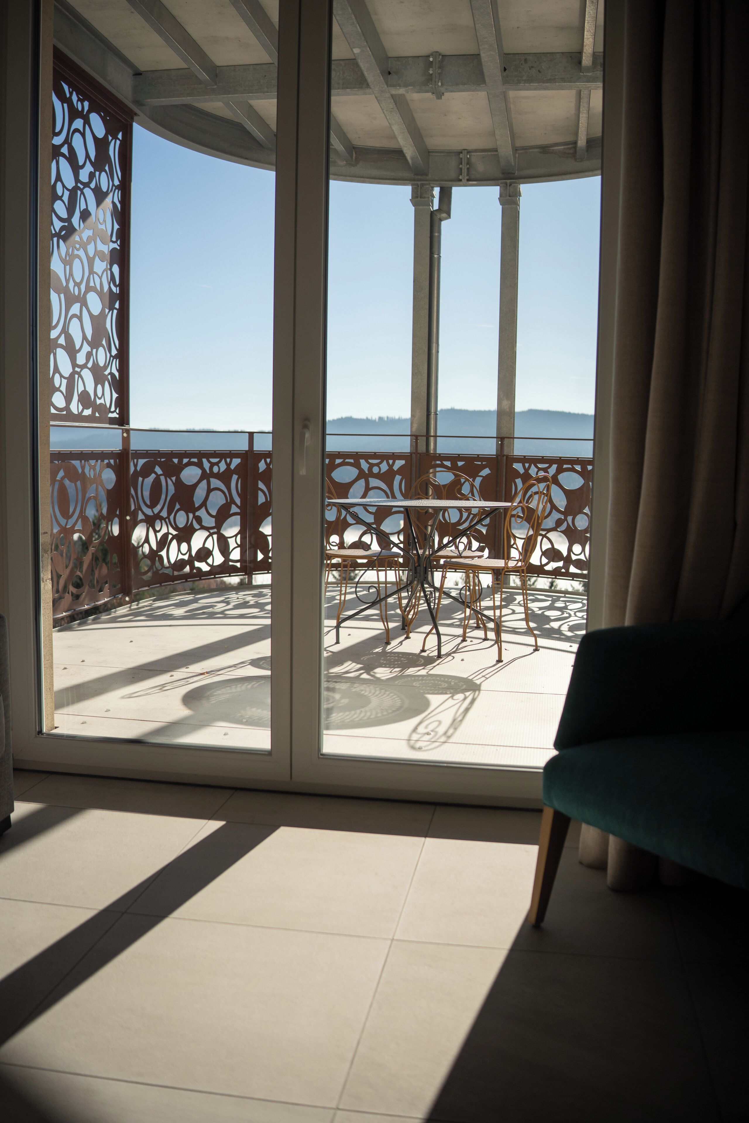 A balcony with a table and chairs, a view of the sea, and a sofa inside a room.