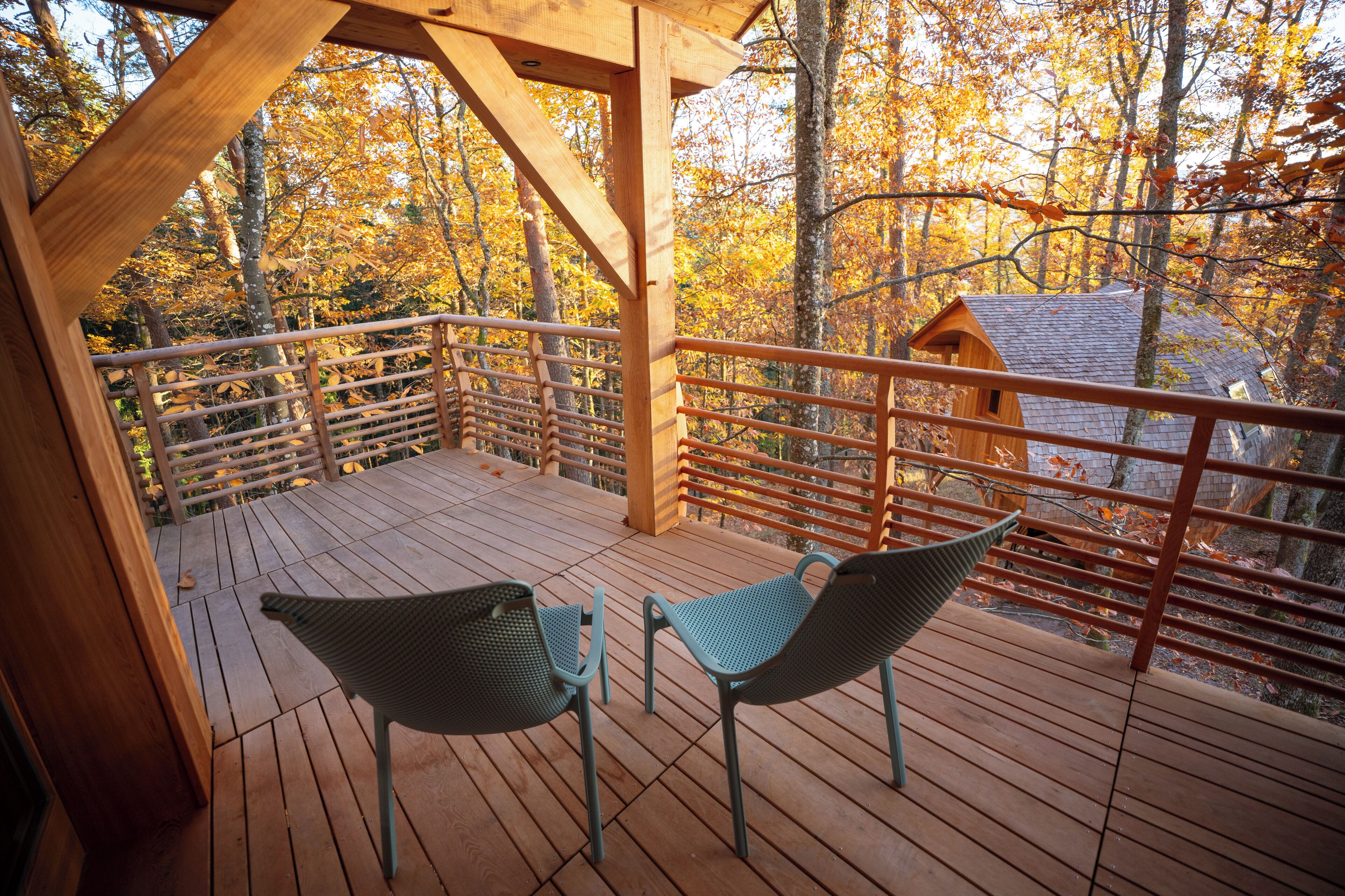 A wooden deck with two chairs and a wooden structure in the background.