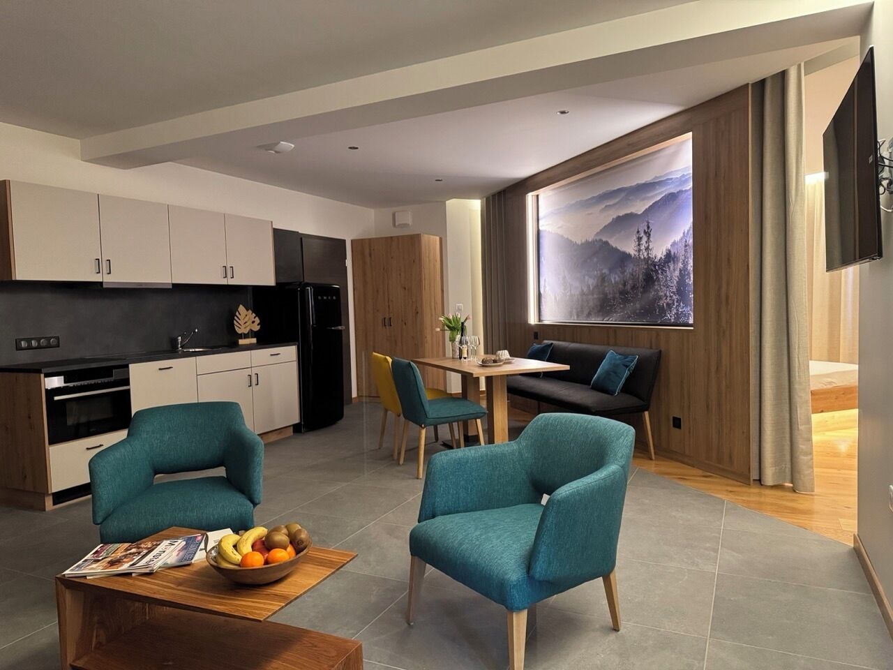 A modern living space with teal armchairs, a dining table, and a kitchen area.