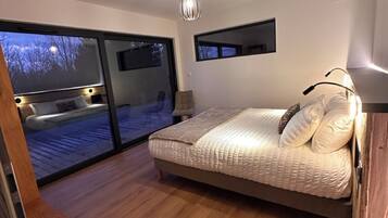 Een slaapkamer met een groot bed, een plafondlamp, uitzicht door het raam en een houten vloer.