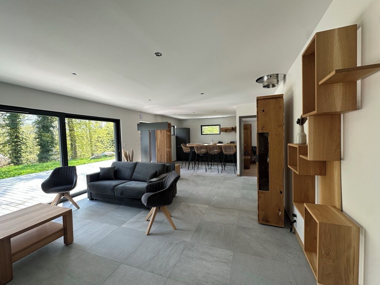 Un salon moderne avec un canapé gris, une table basse en bois et un coin repas équipé d’un téléviseur.