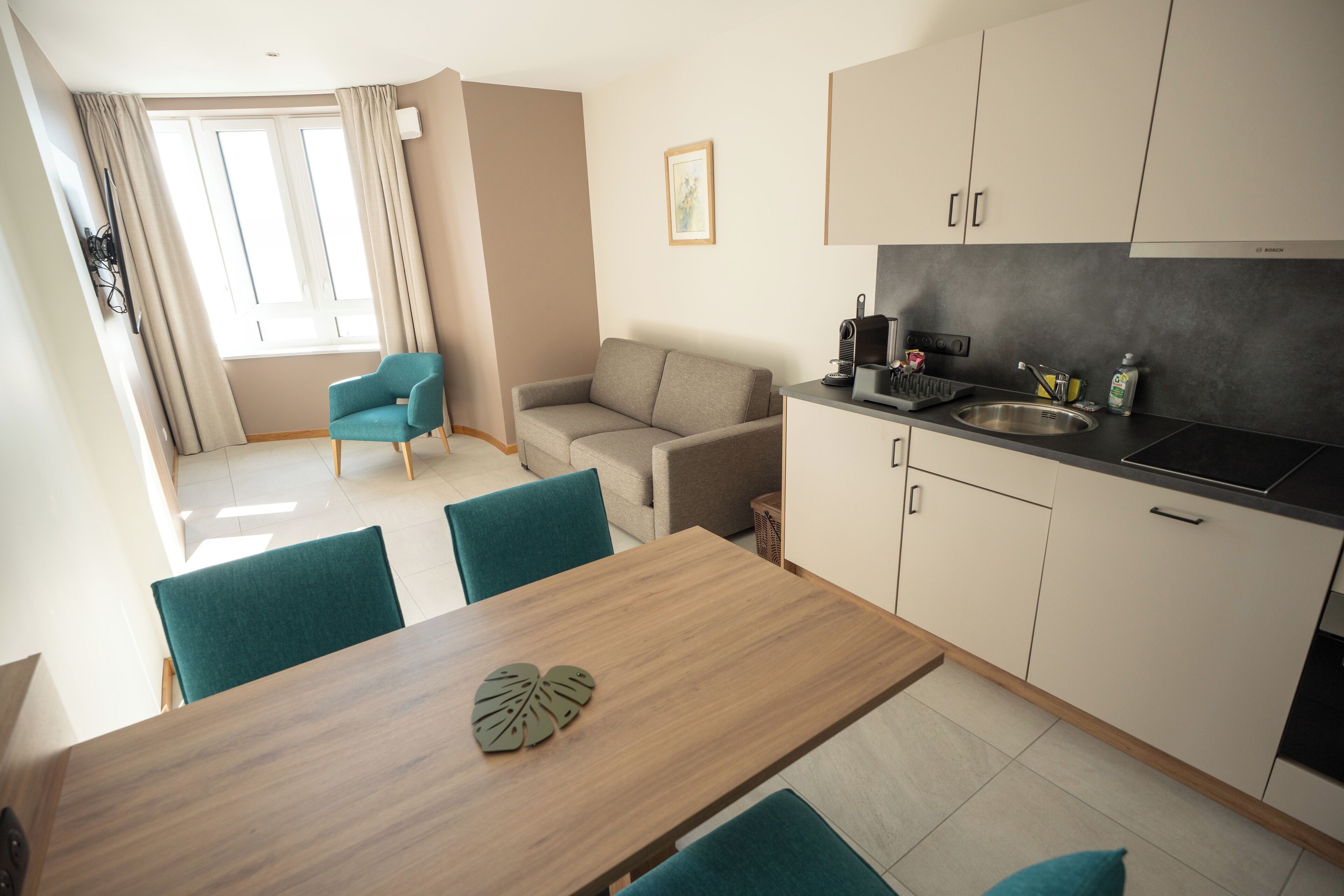 Une cuisine moderne avec un coin repas, comprenant une table en bois, des chaises de couleur turquoise et un canapé.