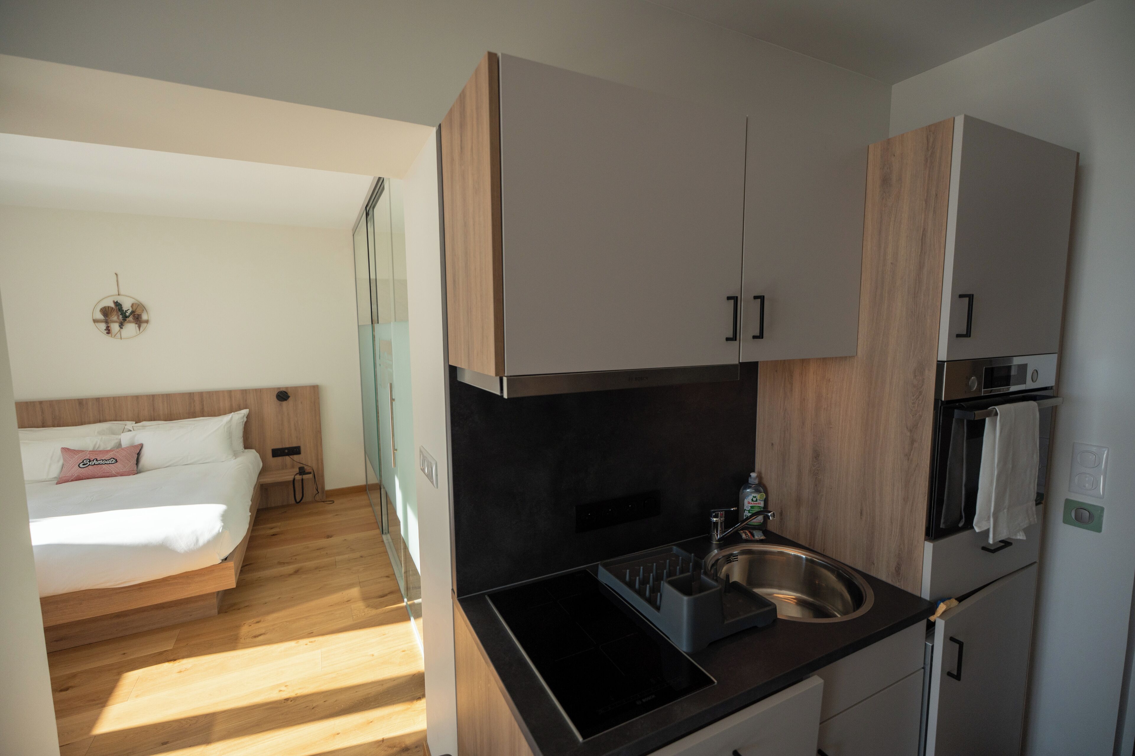 Et kompakt hotelværelse med tekøkken, en seng med trægavl og et lille natbord.
