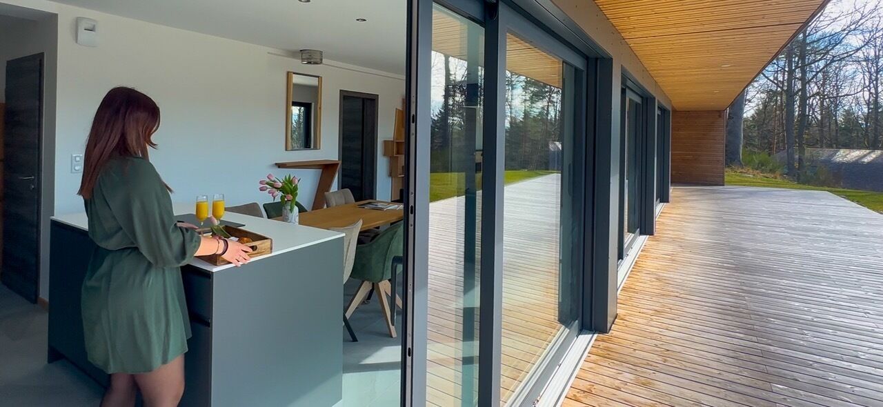 A modern kitchen with a woman preparing food, a dining area with a table and chairs, and a large sliding glass door leading to an outdoor deck.