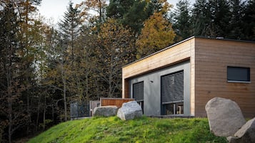 Un bâtiment moderne avec une façade en bois, de grandes portes de garage et une colline verdoyante parsemée de rochers.