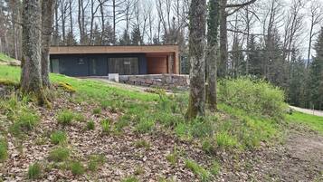 Uma casa moderna com base de pedra e exterior de madeira, cercada por uma área arborizada.