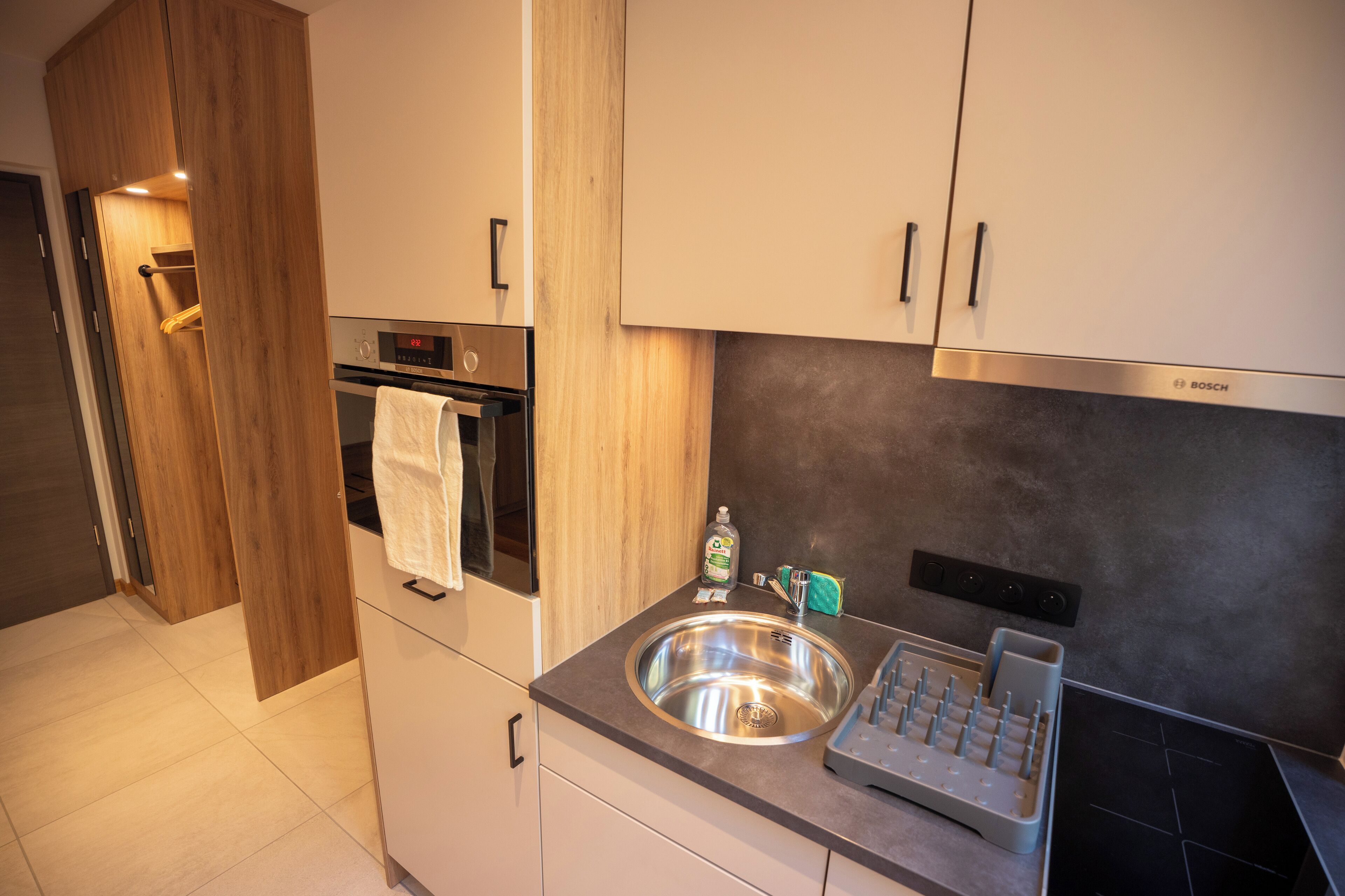 A modern kitchen with a stainless steel sink, a Bosch oven, and wooden cabinetry.
