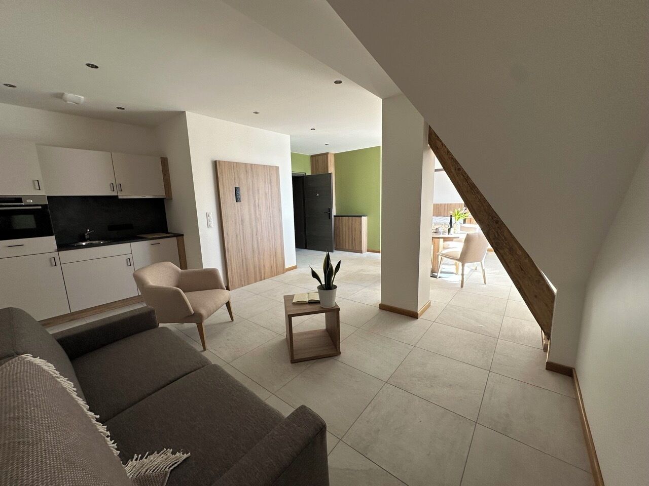 Una sala moderna con un sofá, una silla, una mesita con una planta y una escalera que lleva a otra habitación.