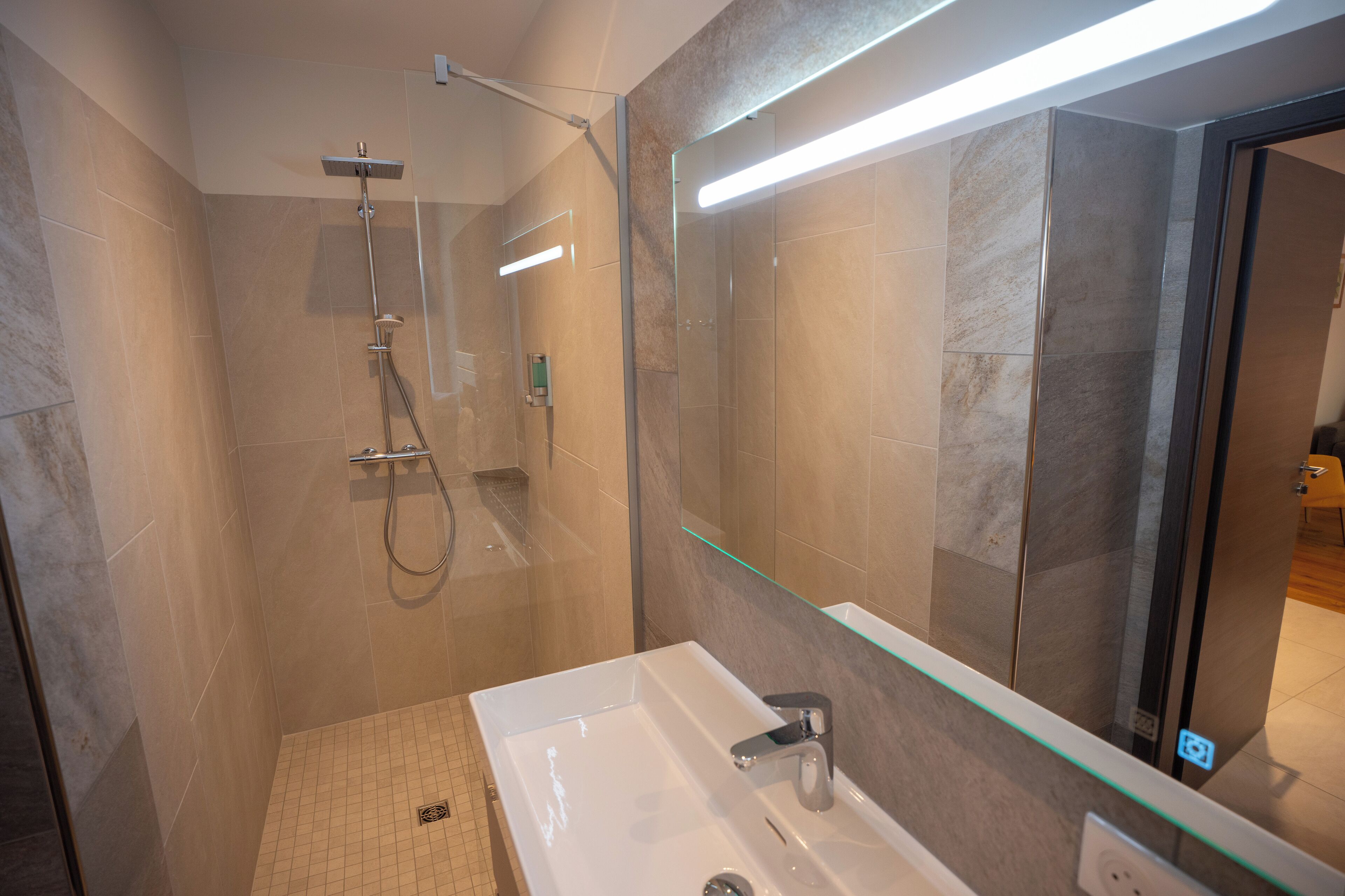 Une salle de bain moderne avec une douche à parois de verre, un grand miroir et un lavabo blanc.
