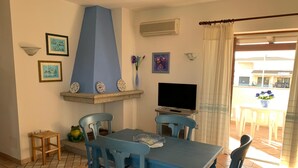 Un comedor con una mesa y sillas azules, un televisor y un estante decorativo con platos.
