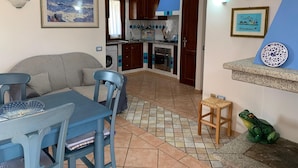 Una sala de estar con sofá y mesa de comedor, una cocina con alacenas de madera y lavadora, y piso de baldosas.