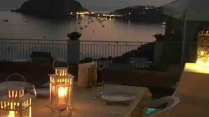 Una terrazza con vista sul mare, arredata con un tavolo e sedie, e due lanterne accese.