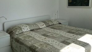 Una camera da letto con un letto ricoperto da una coperta a motivi decorativi, un comodino bianco e una lampada fissata alla parete.