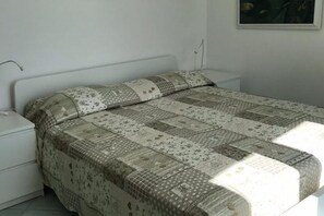 A bedroom with a bed covered in a patterned quilt, a white nightstand, and a wall-mounted lamp. - The Fig Tree "Villa Nunzia" (Barano D'ischia)