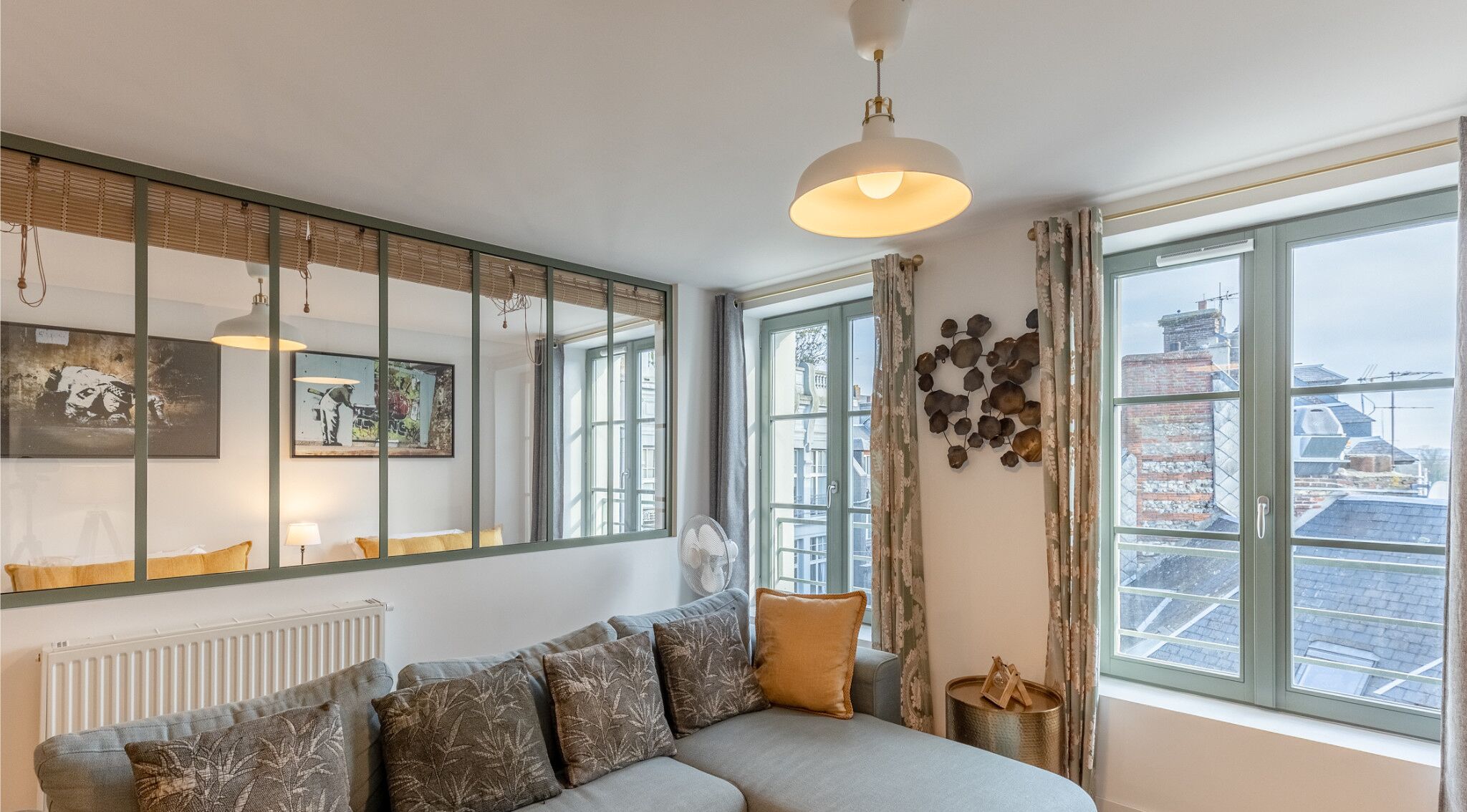 A modern living room with a sofa, a large mirror, and a view of the city through the windows.