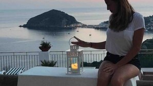 A person sitting on a balcony overlooking a body of water with a distant island and boats. - Olive Tree "Villa Nunzia" (Barano D'ischia)