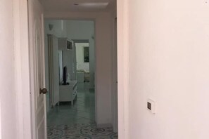 Un corridoio stretto con un pavimento decorato che conduce a una stanza con un letto e una cassettiera.